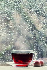 Cup of hot black tea on the blurred background of wet window on