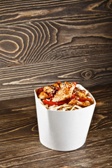Delicious wok noodles box container with udon and chicken on wooden table. Chinese and asian takeaway fast food. 