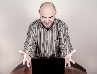Angry and nervous businessman making a grimace, gesticulating with his hands and looking at a laptop