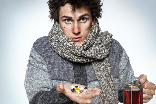 Ill man taking many pills. Young guy holding many pills and hot tea. Medication or drugs abuse, healthcare concept