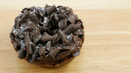 The dark chocolate donut (doughnut) on the wooden board.