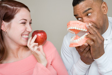 Dentist and woman holding an apple and false teeth