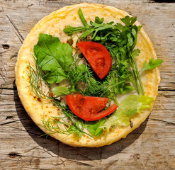 Russian pancakes with fresh herbs and slices of tomato on a wooden background