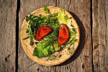 Russian pancakes with fresh arugula and parsley and pieces of tomato on a wooden planks