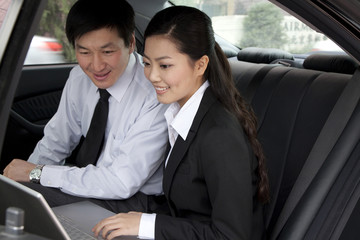 Businesspeople working on laptop in back of car
