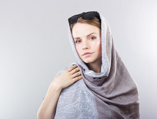 beautiful young woman in an embroidered shawl and sunglasses on a gray background
