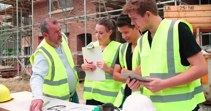 Builder On Building Site Discussing Work With Apprentices