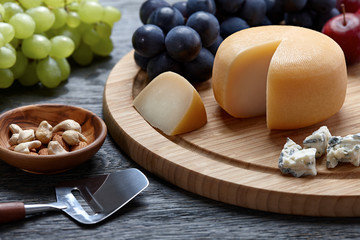 Round cheese with grapes on wooden backround