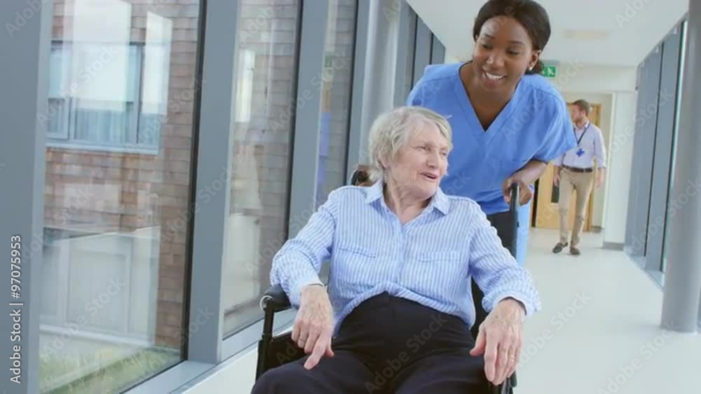 Wall mural Nurse Pushing Senior Patient In Wheelchair Along Corridor