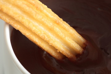 cup of liquid chocolate and churros on a wooden table