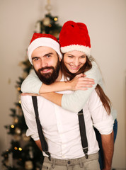 Joyful couple in red hats on the background of Christmas tree