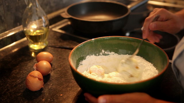 A process of making dough for pancakes: flour being mixed with eggs