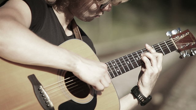 Bleak footage of a long-haired guitarist playing a song in simple chords