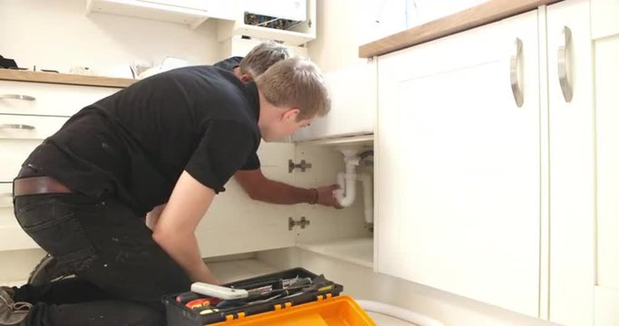 Plumber teaching apprentice to fix kitchen sink
