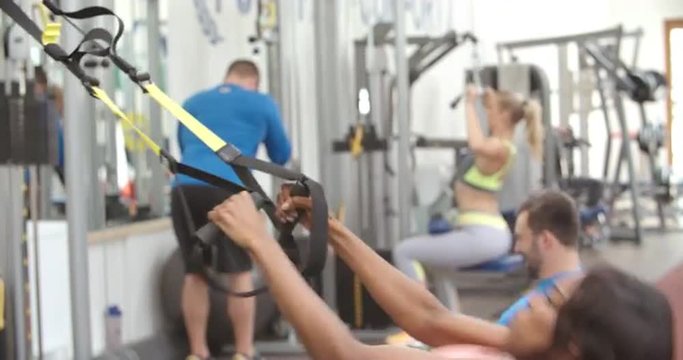 Young woman training with resistance straps in a busy gym