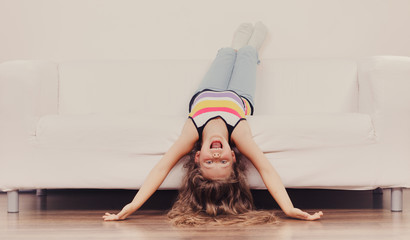 Little girl kid with long hair upside down on sofa