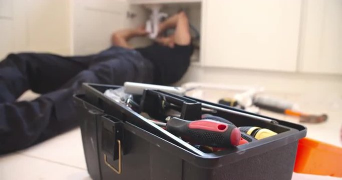 Plumber fixing sink in kitchen, focus on toolbox