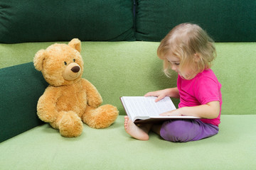 Little girl reading a book Teddy bear.