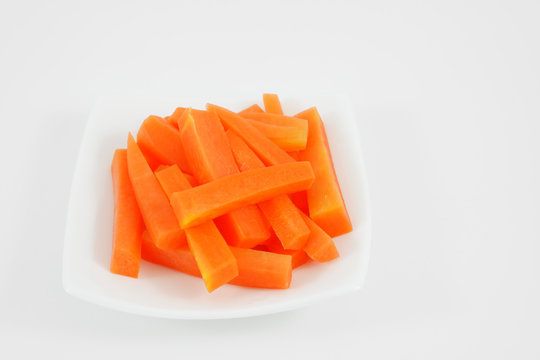 The fresh orange carrot sticks on the white small dish.