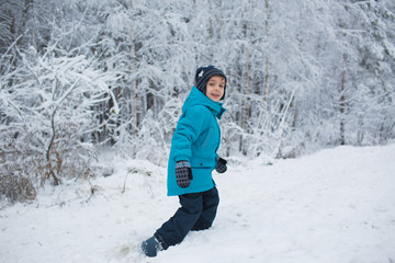 Fototapeta na wymiar A cute little boy walks in a snow in park in the winter