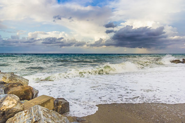 Rocky beach with sea view, waves of water and dark clouds on sky