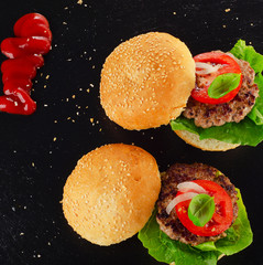 Two Homemade burgers with tomato sauce on dark background.