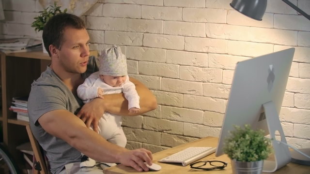 Young father rocking his adorable baby son while working on computer at home