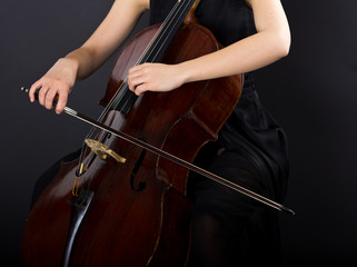 A young girl plays the cello in the dark. Hands on cello