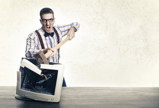 young angry nerd destroying old computer monitor