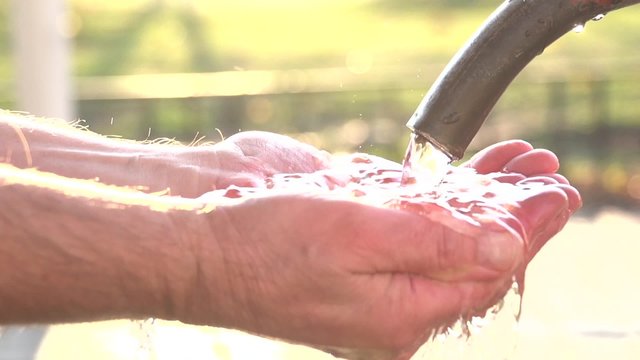 Clean, shining water poured into the man's hands.  Slow motion 240 fps.