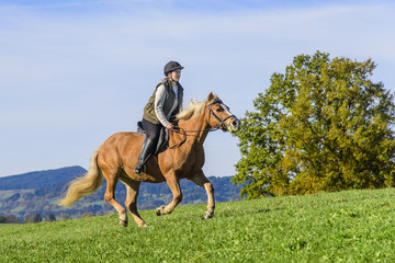über eine Wiese reitende Frau