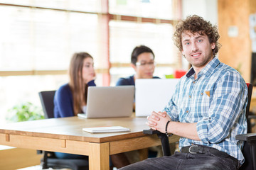 Smiling happy young curly male working in team using notebook