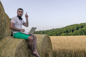 Naklejka na ściany i meble Man with laptop sitting on a stack of hay and shows thumb up