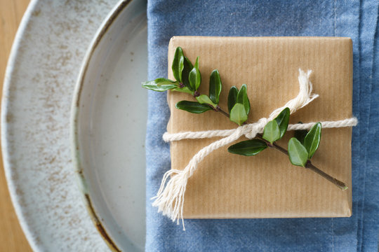 Detail of place setting decor: simply wrapped present decorated with green branch and twine on the blue napkin