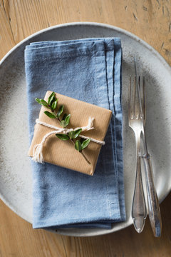 Place setting decor: simply wrapped present decorated with evergreen branch and twine on the blue napkin