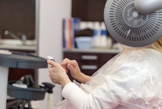A blonde woman surfing the internet with her smartphone in hair studio