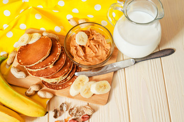 
hearty and healthy breakfast , American pancakes with bananas , nuts , peanut butter and milk on a wooden background