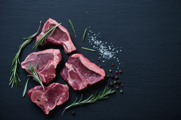 Top view of raw T-bone lamb steaks on a black wooden surface