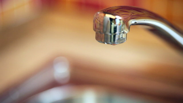 Closeup of water dripping from a kitchen tap -  water wasting concept