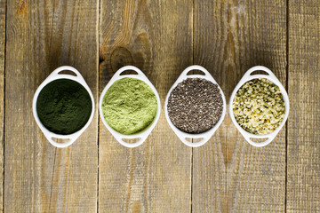 Fototapeta na wymiar Superfood raw seeds and powder. Body building powders and health food on wooden background. Superfood served in small bowls.