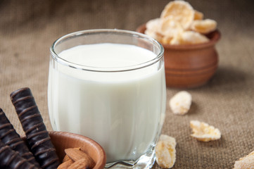 A glass of milk with almond nuts, corn flakes, chocolates,  on sacking burlap back ground 