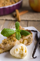 Apple pie with ice cream, decorated with vanilla, mint and cinnamon on wooden background. A delicious piece of cake with ice.