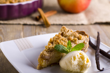 Apple pie with ice cream, decorated with vanilla, mint and cinnamon on wooden background. A delicious piece of cake with ice.