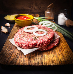 raw cutlet for burger on cutting board with sauce, onions on wooden rustic background close up