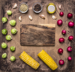 Fresh vegetables ingredients radishes, brussels sprouts, corn, seasoning lined around the cutting board on wooden rustic background top view place for text