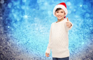 Obraz premium smiling happy boy in santa hat showing thumbs up