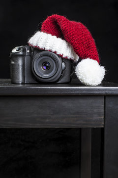 DSLR camera in a red Christmas hat of Santa Claus standing on a black wooden table