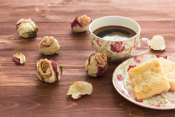 rosebuds and a mug of coffee and cake on a dark wooden background