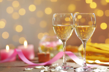 Glasses of wine, white roses and candles, on blurred background
