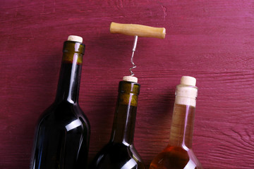 Three bottle wine and corkscrew on purple wooden background